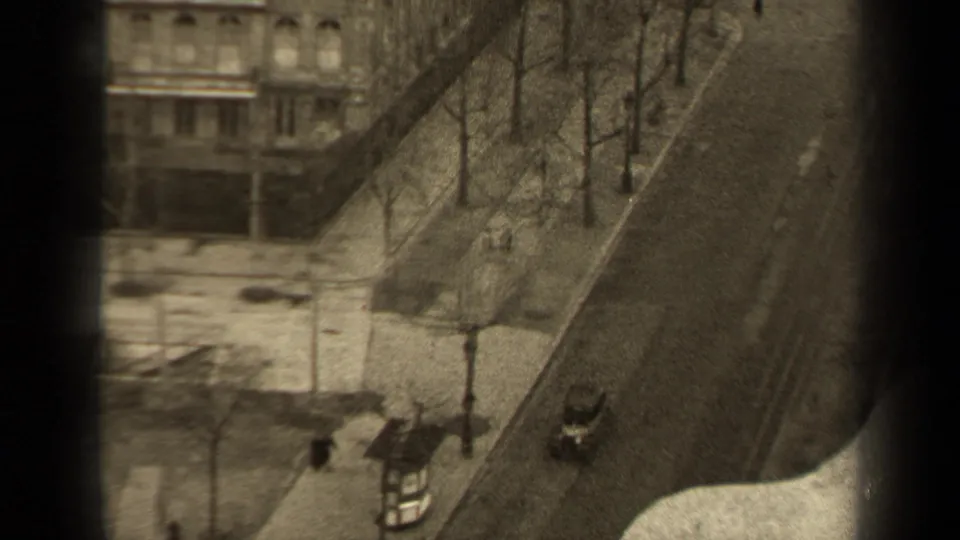 A high-angle 1947 Paris street view shows a vintage car passing below bare trees and pedestrians near stone buildings.