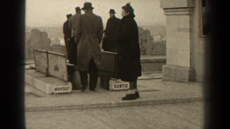 1947 Paris 8mm frame showing adults in overcoats and hats gathered at a bilingual exit marked WAYOUT and SORTIE.