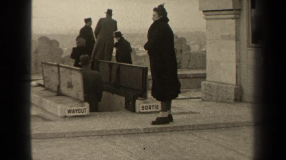 1947 Paris frame showing several coated figures around a public exit barrier with bilingual signage.