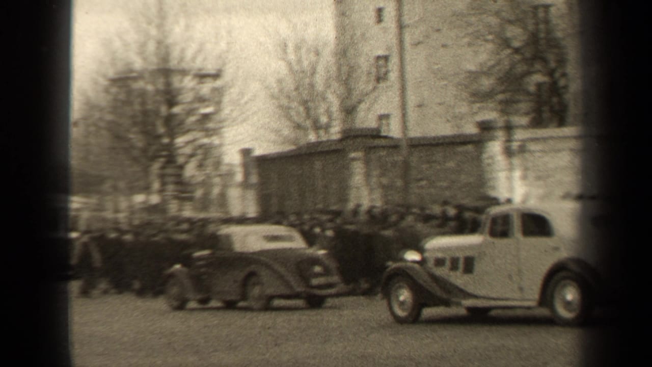Classic cars move through a busy city street with pedestrians and bare trees.