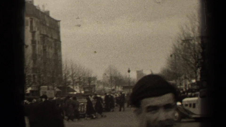 Pedestrians in coats cross a broad Paris street in 1947, with bare trees, tall buildings, and a classic car at the edge of frame.