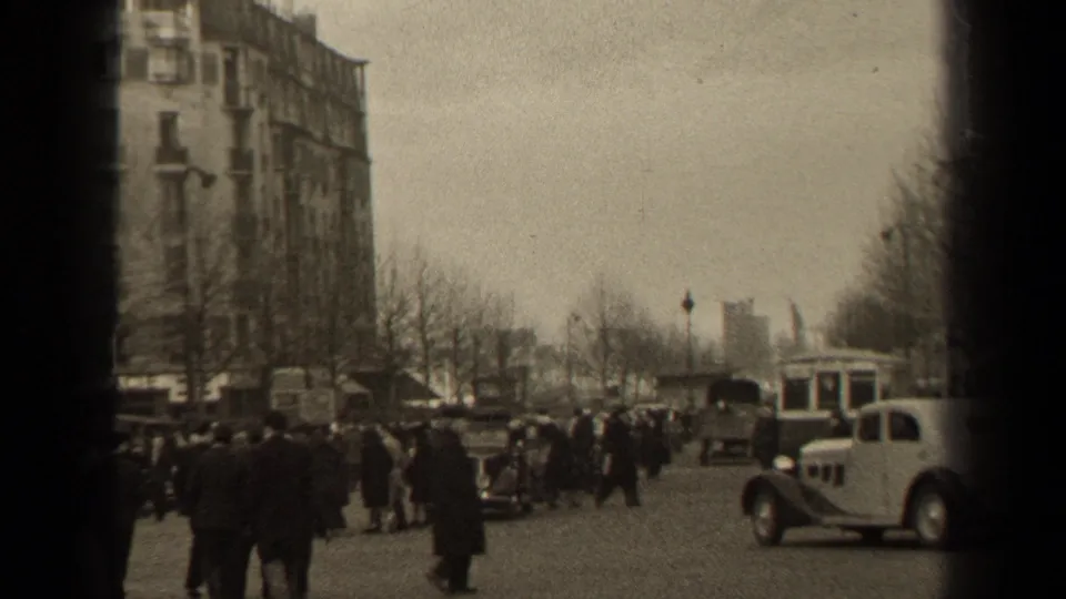 1947 Paris street scene with pedestrians, classic cars, a tram or bus, bare trees, and tall buildings under an overcast sky.