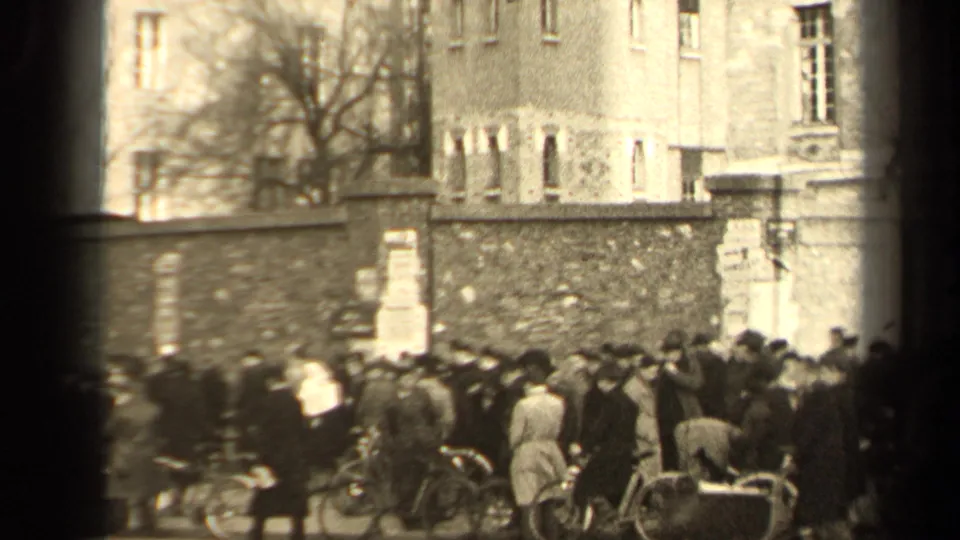 1947 Paris crowd scene with pedestrians and bicycles along a stone wall near multi-story buildings.