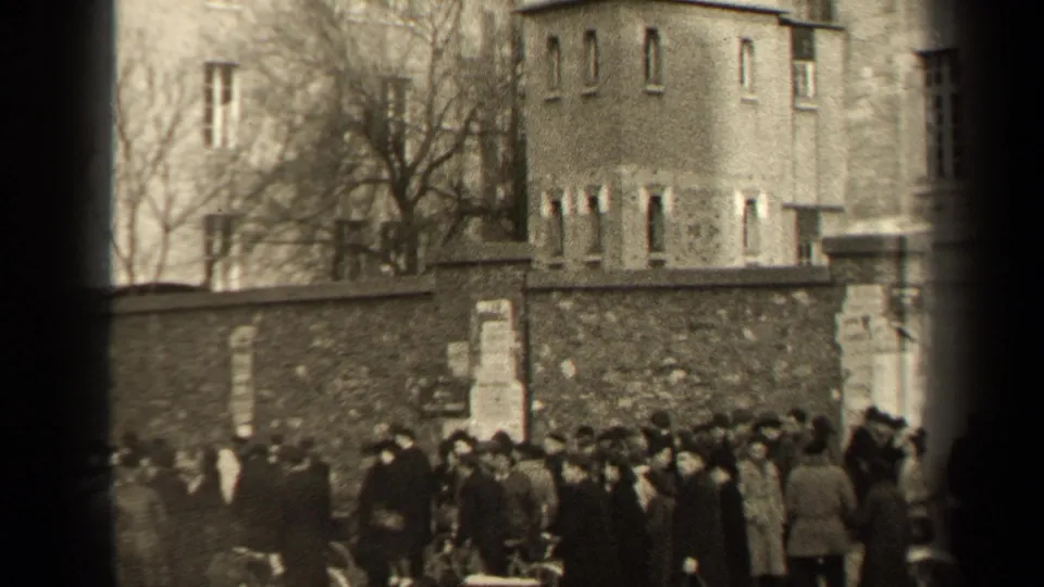 1947 Paris street view with a dense group of pedestrians gathered beside a stone wall and buildings.