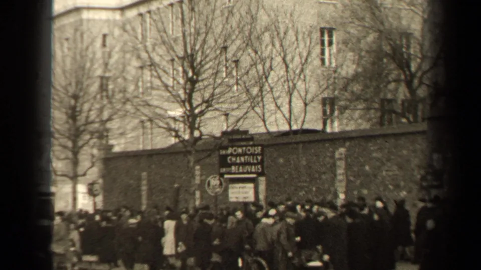 1947 Paris street crowd near a roadside sign reading Pontoise, Chantilly, Beauvais, with buildings and bare trees behind.