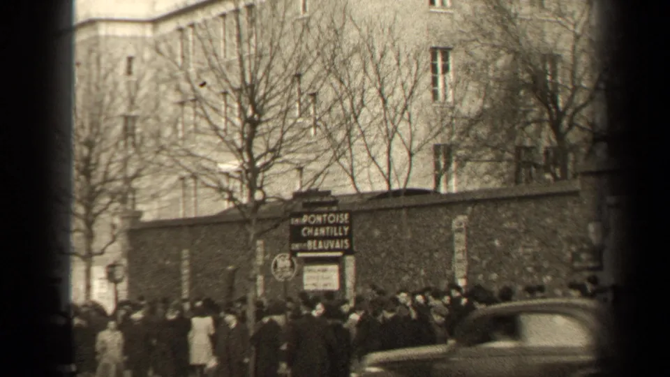 1947 Paris street scene with a passing car, pedestrians, bare trees, and the Pontoise Chantilly Beauvais sign near a wall.