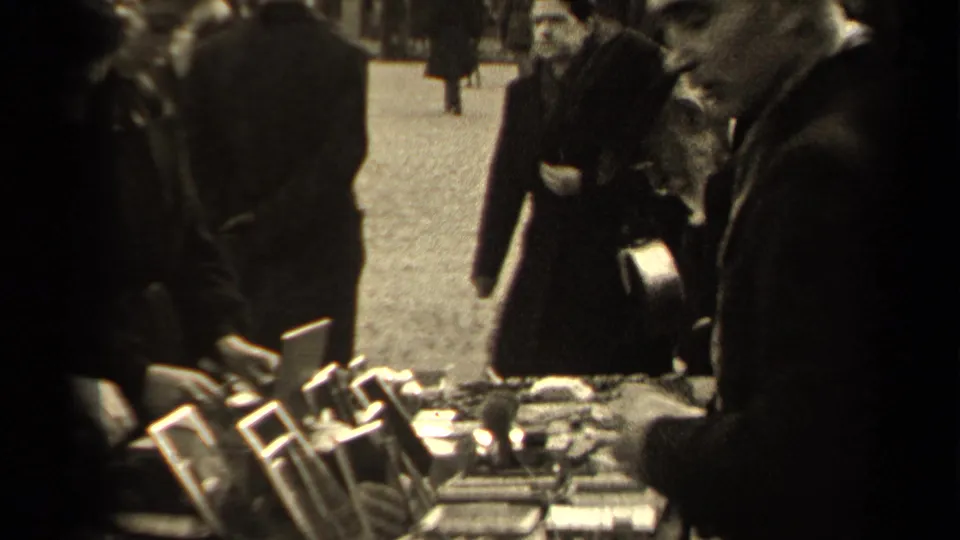 A 1947 Paris flea market table is filled with small mirrors and objects while shoppers and passersby move through the street scene.