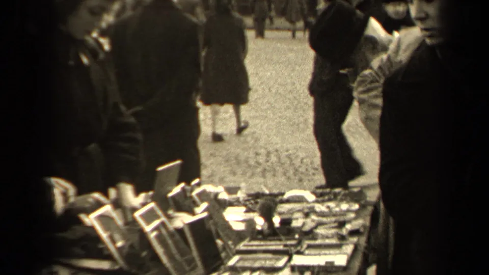 The Paris flea market table shows rows of small mirrors and other goods, with cropped shoppers and pedestrians moving around the stall.