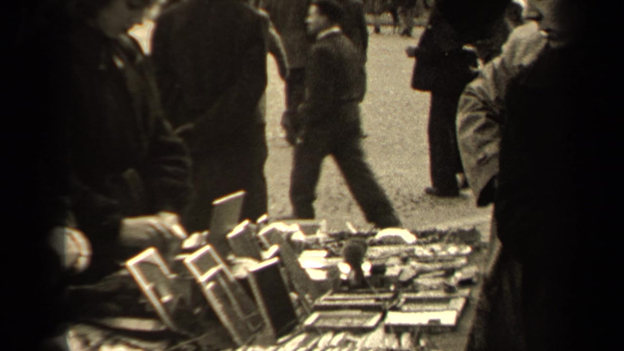 Crowded outdoor market table with small framed goods and pedestrians passing behind it.