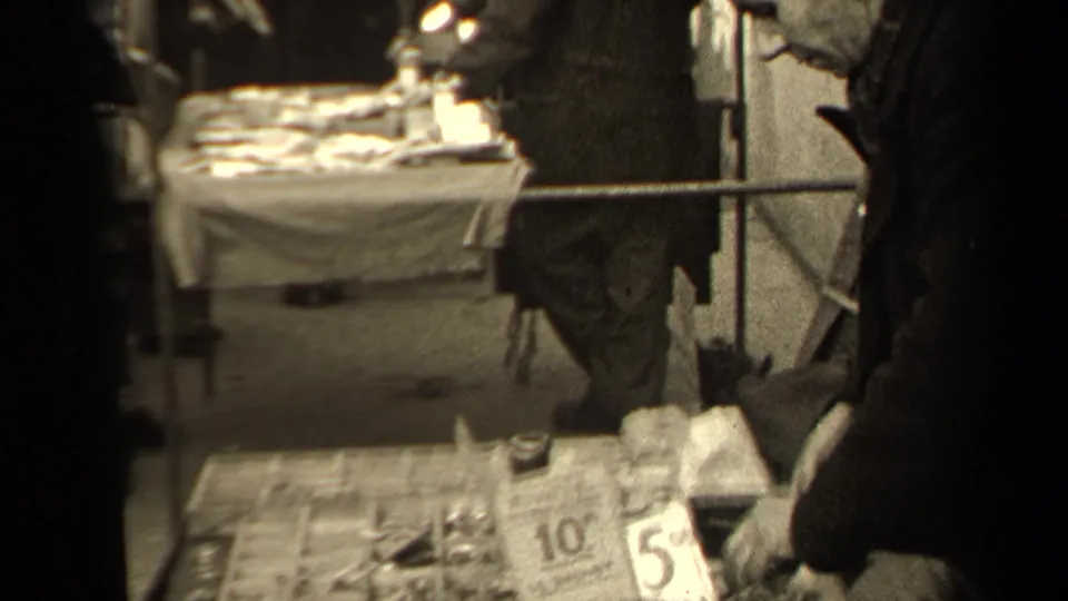 Handheld 1947 Paris market frame with a small-wares tray low in view and a cloth-covered stall table behind.