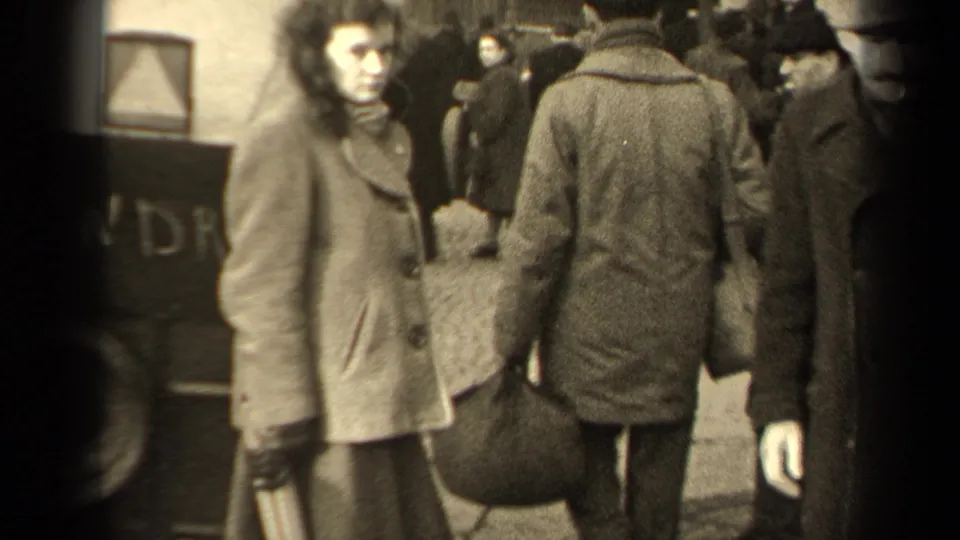 In 1947 Paris home-movie footage, a woman in a heavy coat looks toward the camera as pedestrians pass around her.