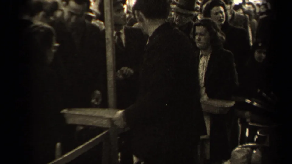 A dense Paris street crowd surrounds a foreground man in a dark coat, while a woman and other adults face the camera area.