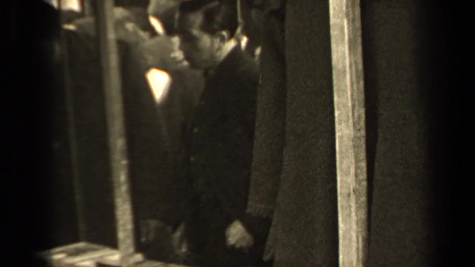 A man in dark formal clothing stands near vertical poles in a grainy 1947 Paris subway or transit scene.