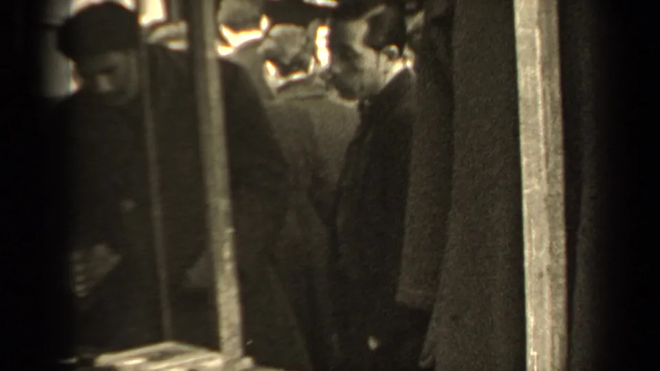 1947 Paris market footage showing shoppers clustered near a stall, partly obscured by dark vertical supports and soft 8mm focus.