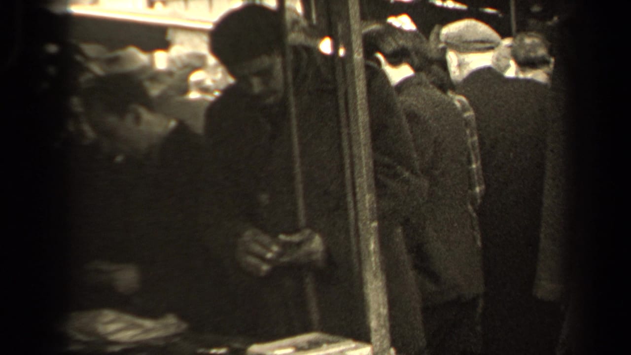 Man in a dark coat and hat looks down while handling small items near a market table.