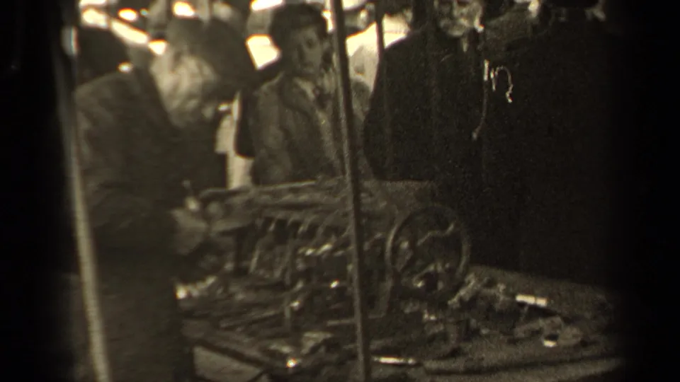 An older shopper leans toward a vendor table with visible metal tools, wheels, and mechanical parts in 1947 Paris market footage.