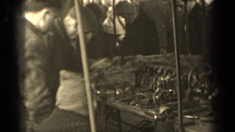 1947 Paris 8mm frame with a man near a polishing bench, visible onlookers, stall poles, and shiny objects on the table.