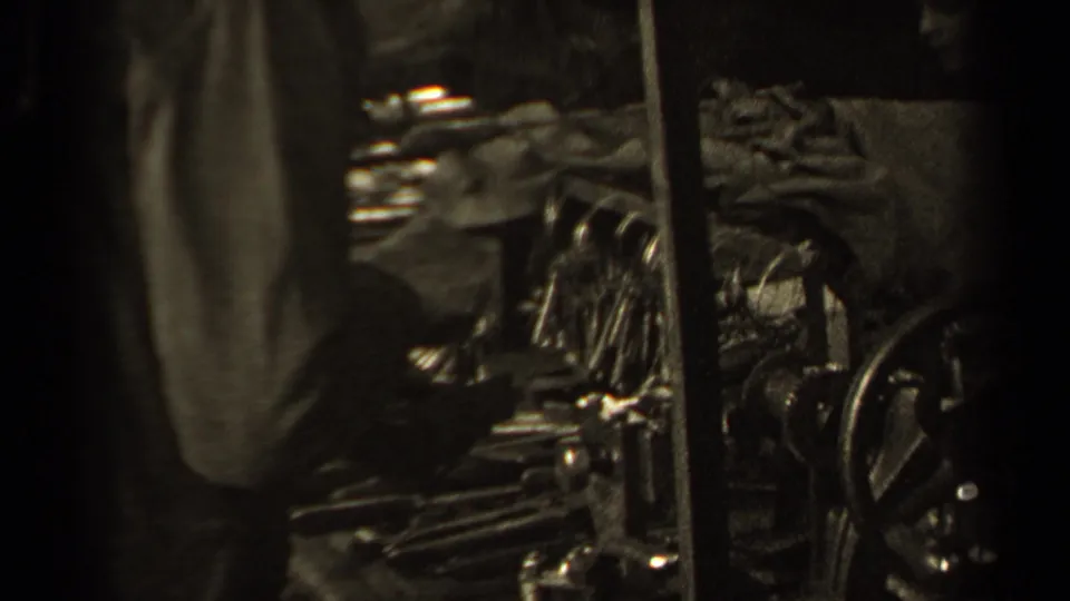 1947 Paris 8mm frame showing a close, dim view of a person’s coat sleeve near dark metal equipment and bundled material.