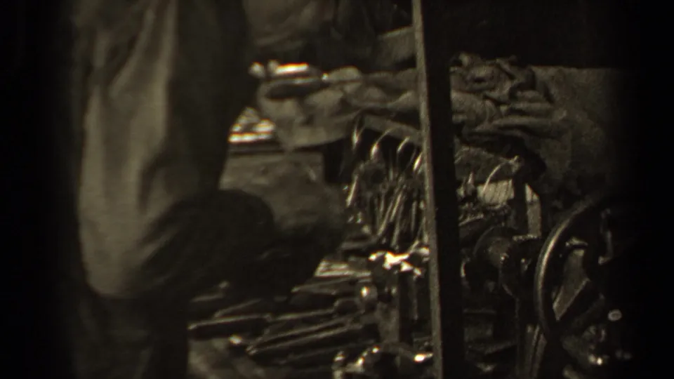 Close 8mm view from Paris in 1947 with a person partly blocking metal machinery and folded or bundled material.