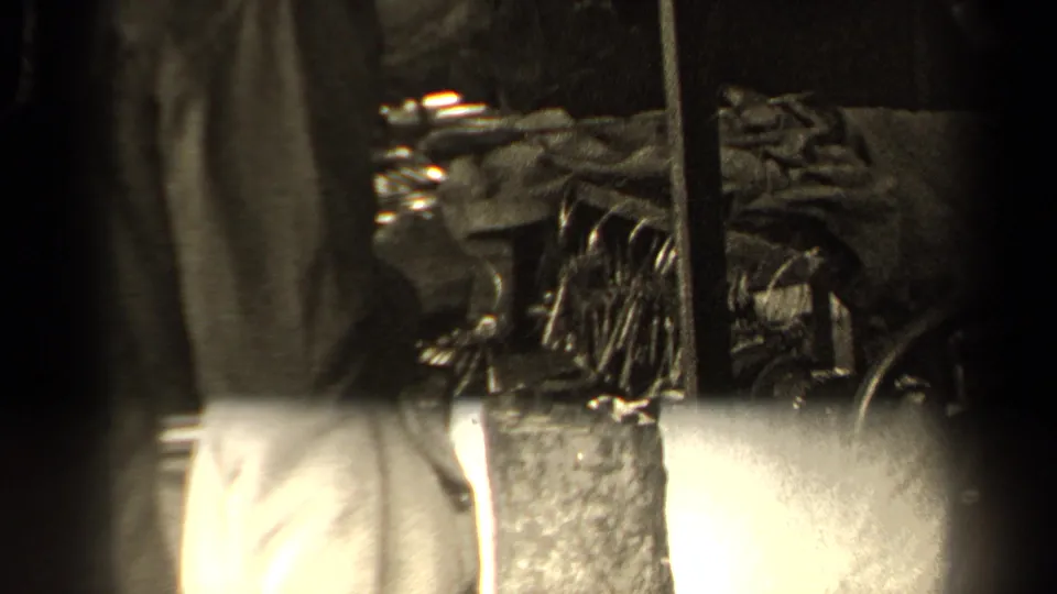 1947 Paris home-movie frame with a coat-clad figure close to metal equipment, stacked items, and a dark vertical edge.