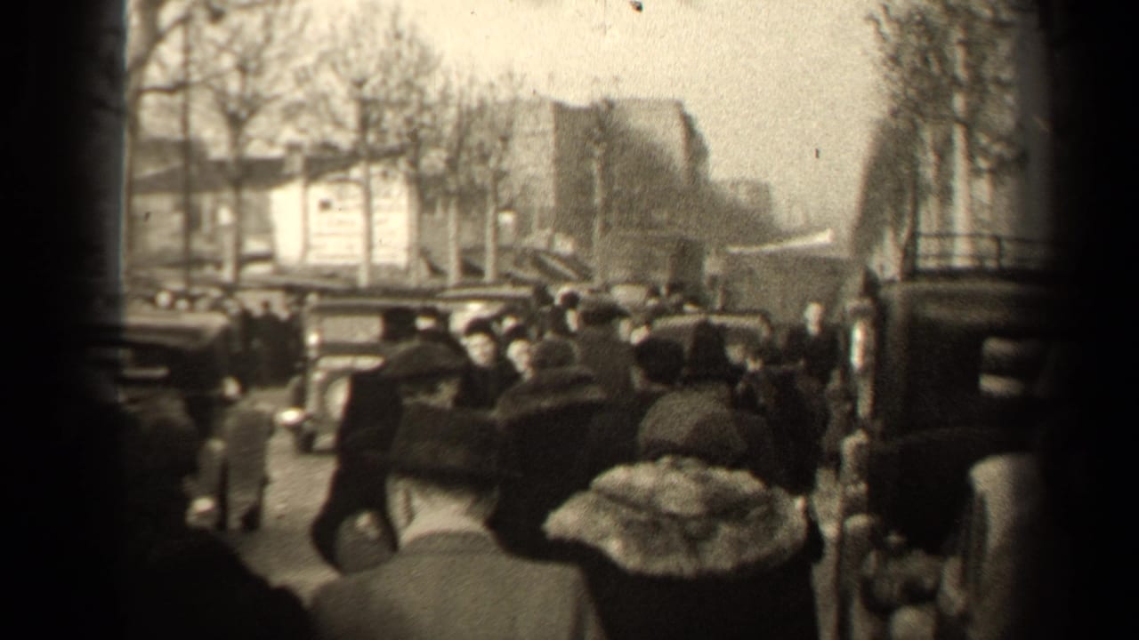 Crowded Paris street with pedestrians in winter coats and vintage cars nearby.