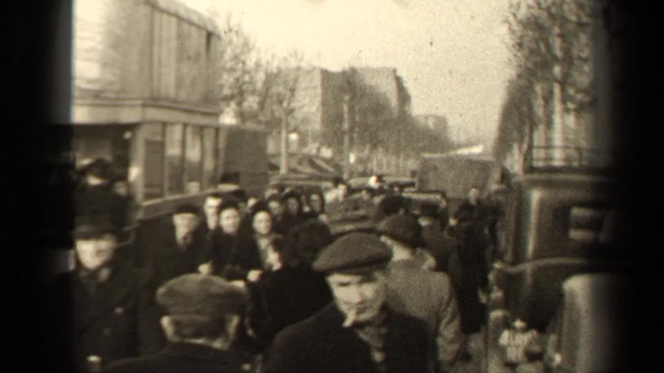 1947 Paris crowd scene with pedestrians in winter dress, a uniformed-looking figure at left, nearby automobiles, and soft 8mm blur.
