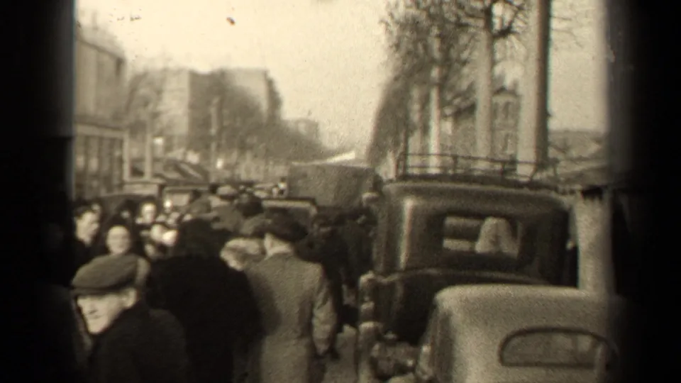 1947 Paris street view with pedestrians in heavy coats gathered near a rounded car, bare trees, and urban building fronts.