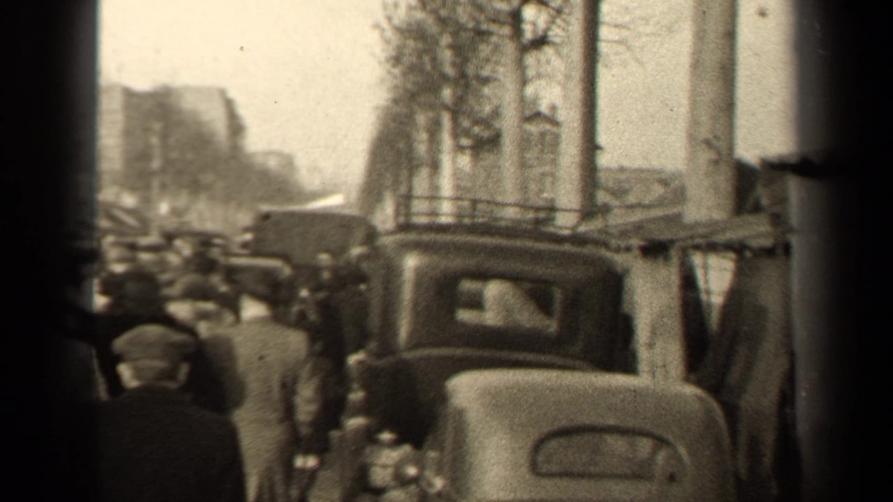 Crowded sidewalk beside older cars, poles, bare trees, and a dark film border.