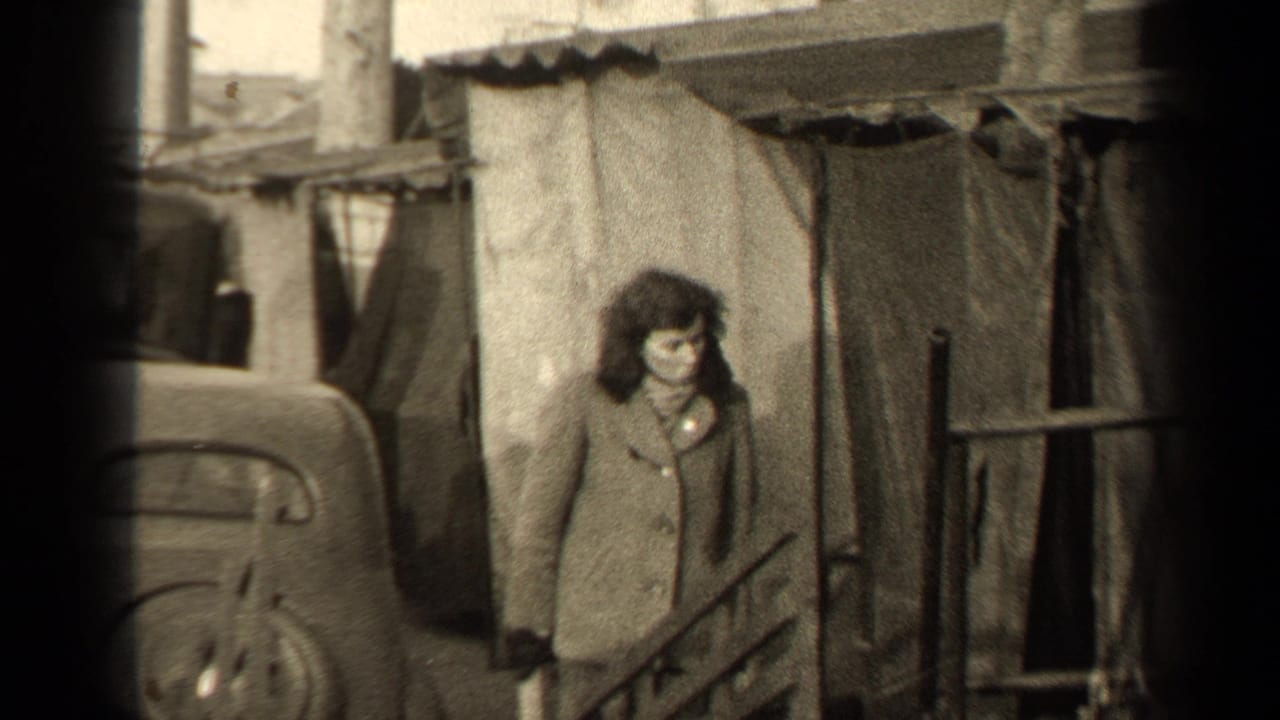 Woman in a buttoned coat stands beside a rounded car on a narrow street.
