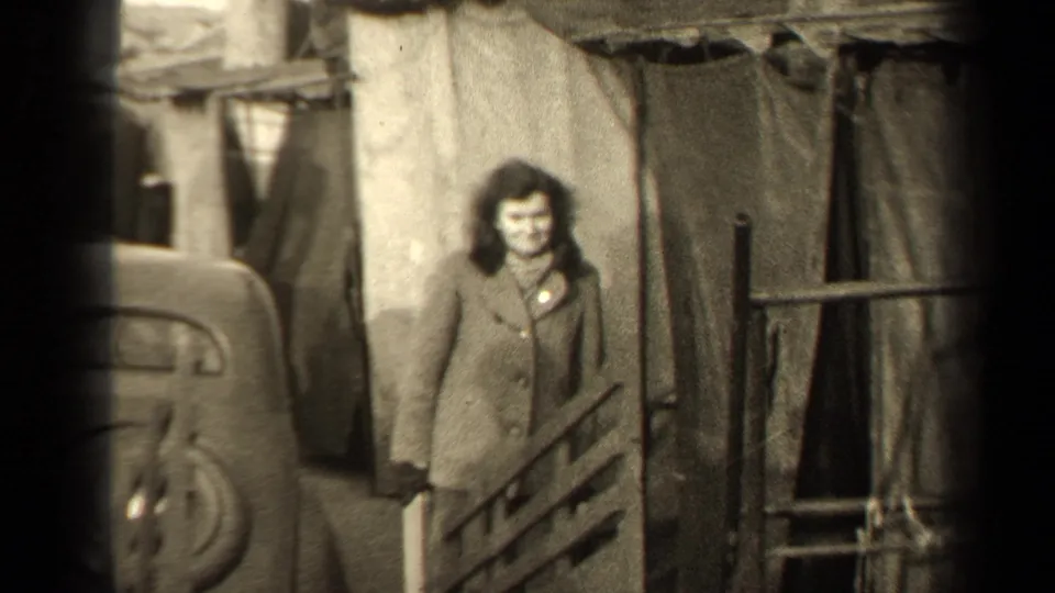 1947 Paris street frame with a woman looking toward the camera beside a car and makeshift-looking coverings.