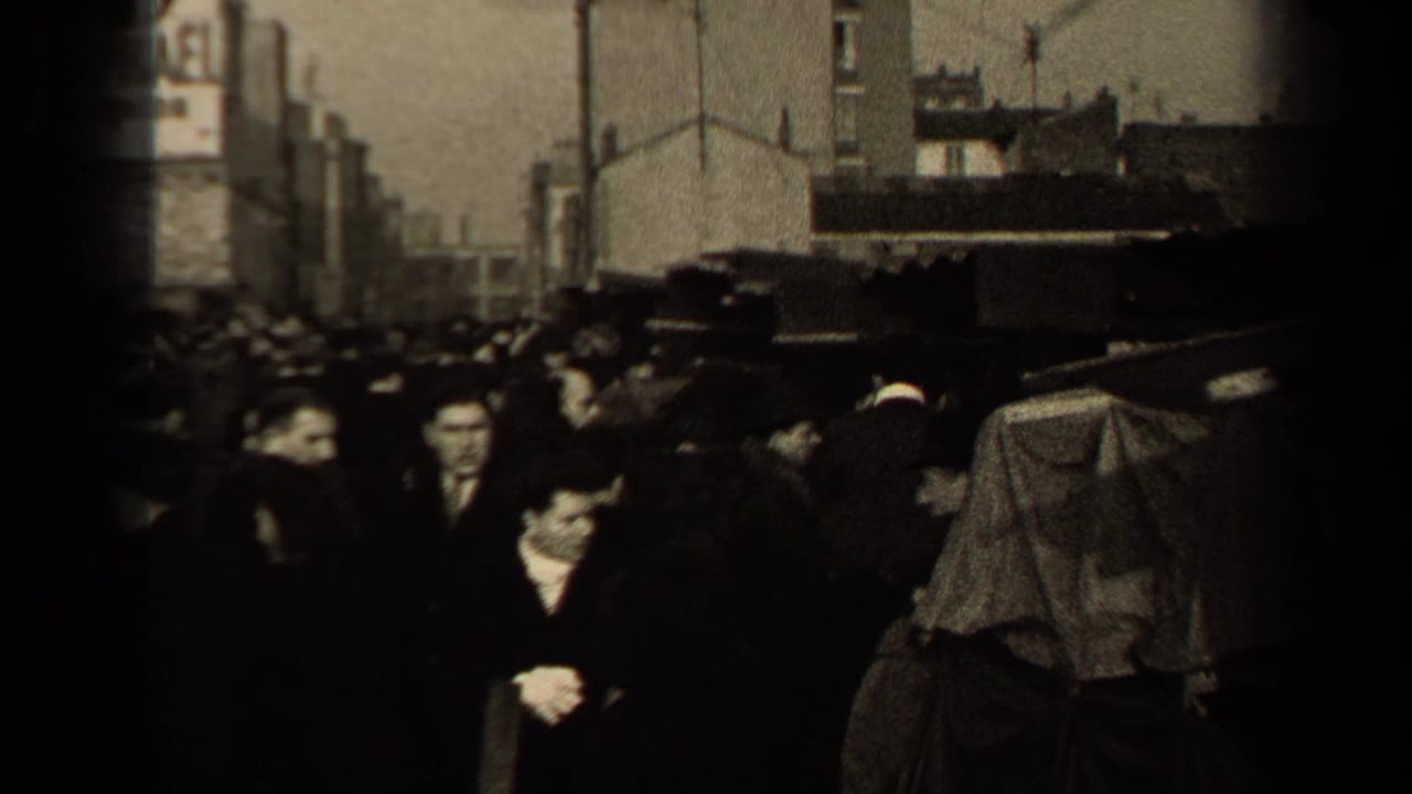 Crowded Paris street with pedestrians in dark coats and hats passing sidewalk stalls.