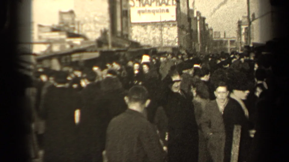 1947 Paris street crowd with dark-coated pedestrians moving past stalls under a partially readable wall advertisement.