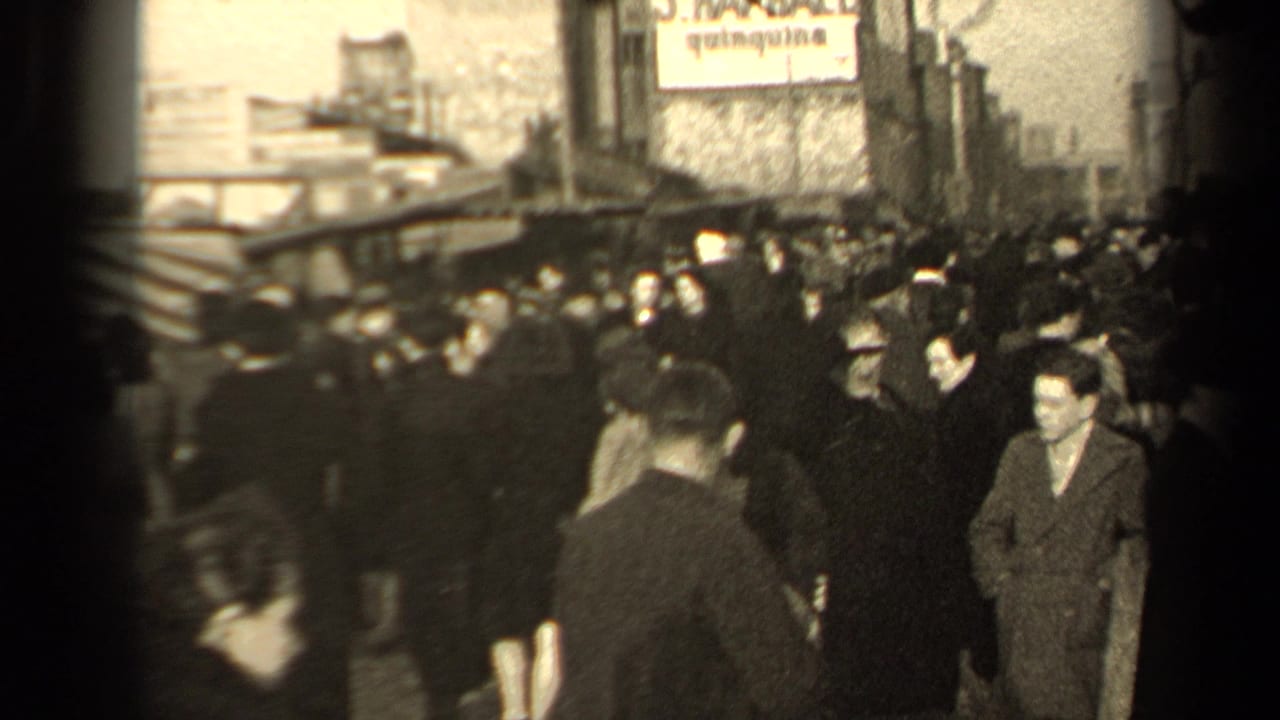 Crowded street scene with pedestrians in coats and hats near striped awnings and a sign overhead.