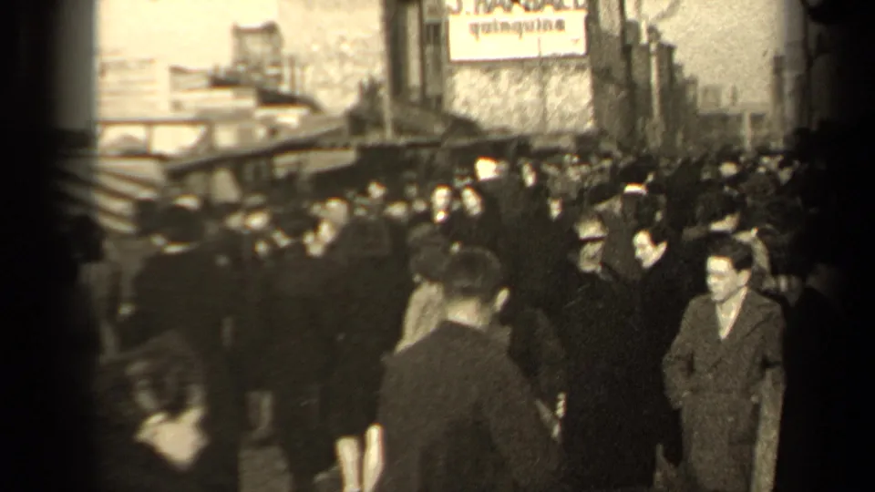 1947 Paris street crowd with men and women in winter coats moving past striped awnings and a visible quinquina sign.