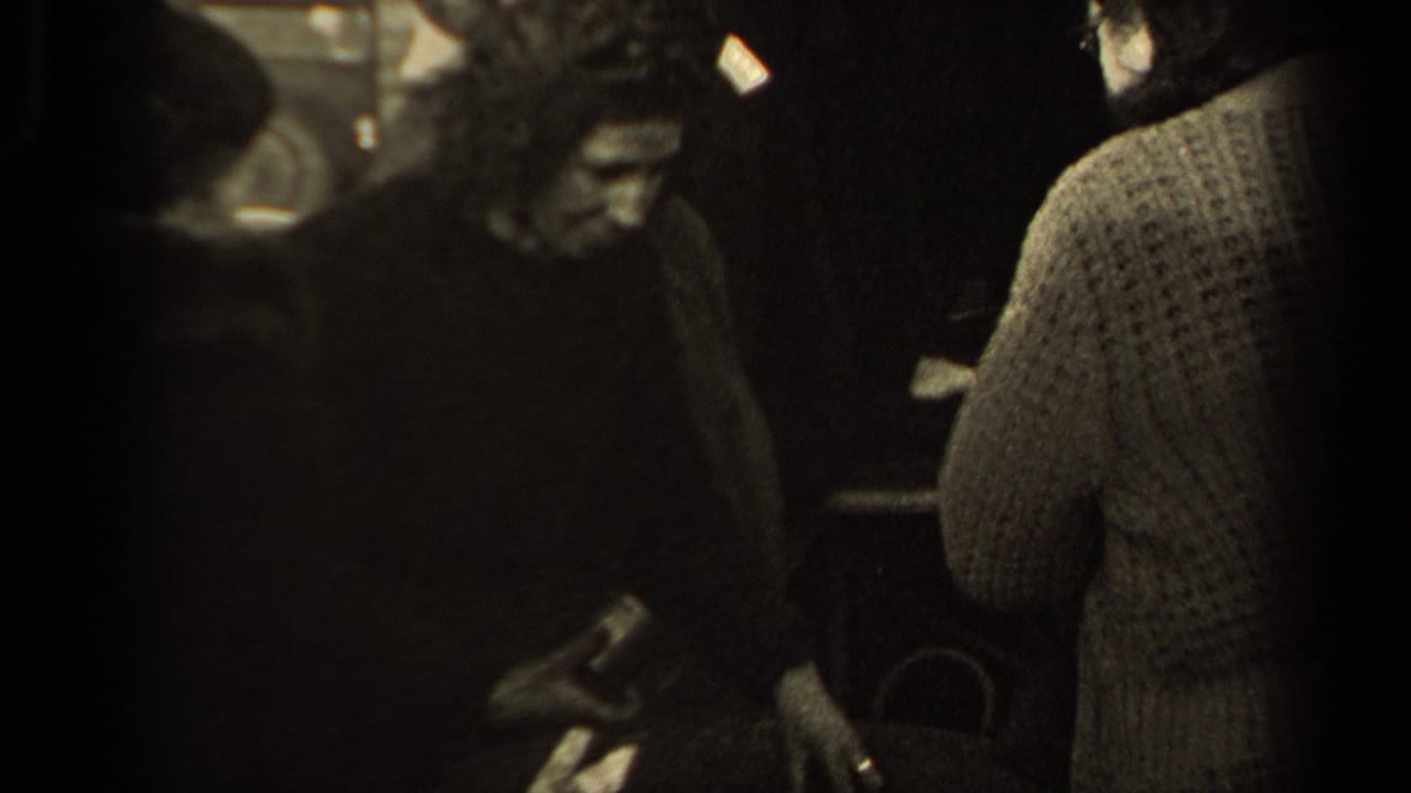 A man in dark clothing and a woman seen from behind in a knit sweater stand near the basket within the crowded 1947 Paris street view.