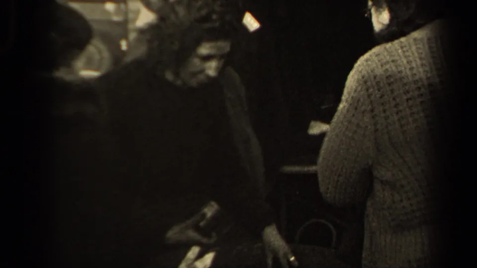 A man in dark clothing and a woman seen from behind in a knit sweater stand near the basket within the crowded 1947 Paris street view.