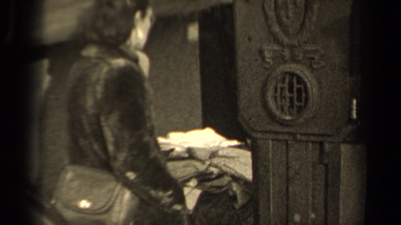 A soft black-and-white frame shows the woman from the side, close to the decorative structure and nearby folded material.