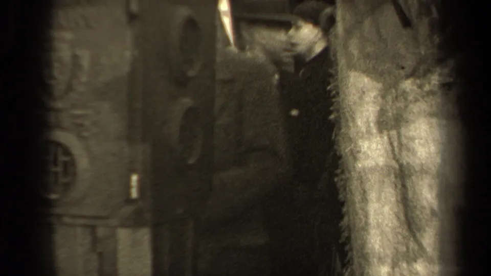 In 1947 Paris footage, adults in winter coats appear beside a wall as a pale garment or cloth is held near the camera.