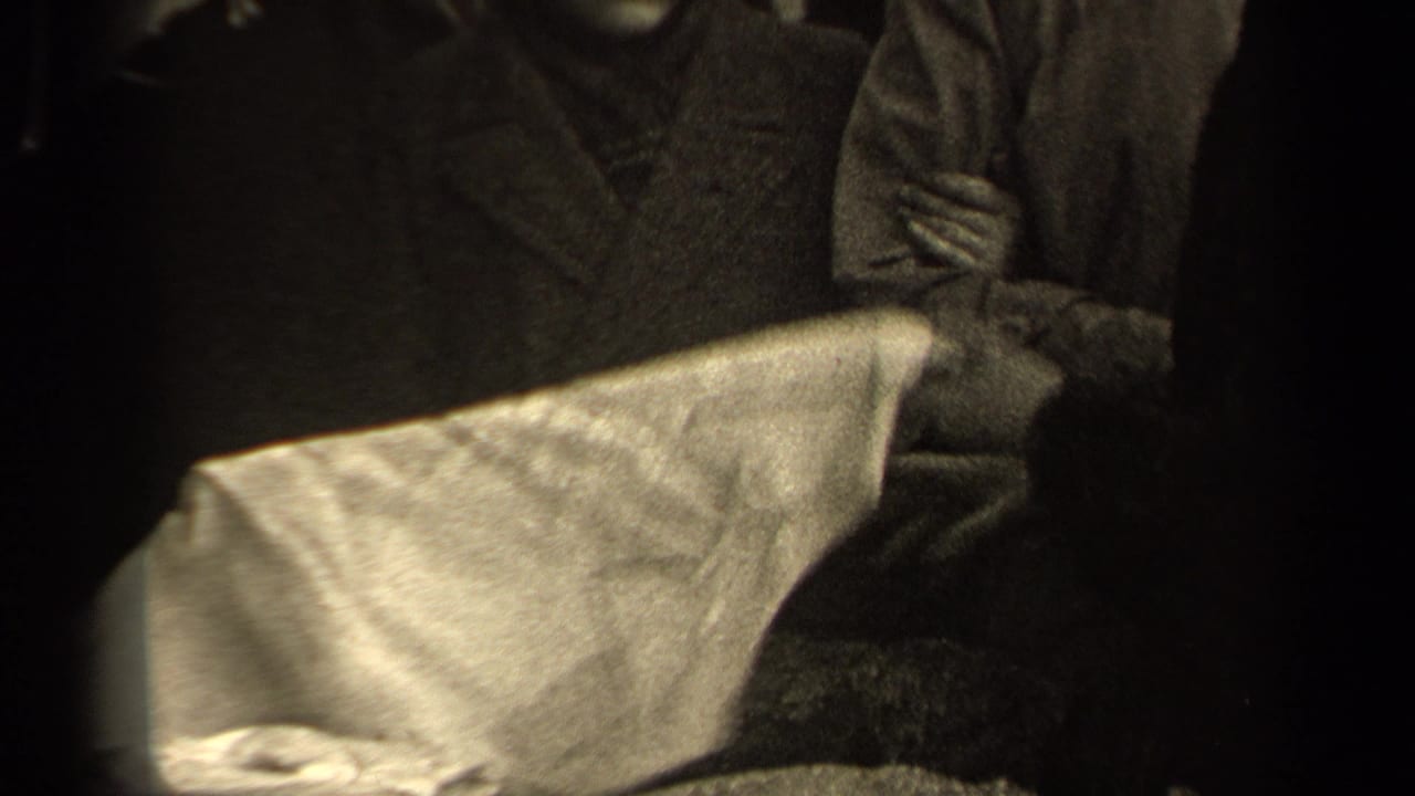 The camera frames a white garment or sheet being handled in front of adults wearing heavy coats on a Paris street.