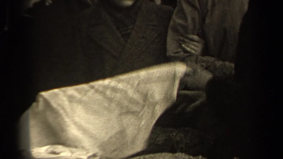 The camera frames a white garment or sheet being handled in front of adults wearing heavy coats on a Paris street.