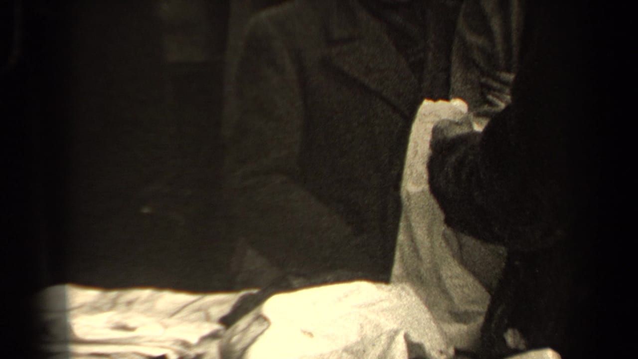 Two people in dark coats handle a light-colored piece of fabric in a dim close-up.