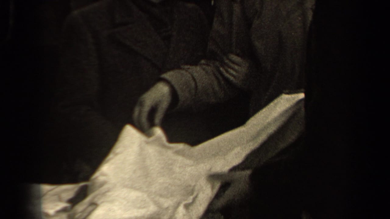 A figure in a long coat holds pale fabric as another hand reaches in, continuing the 1947 Paris fabric inspection.