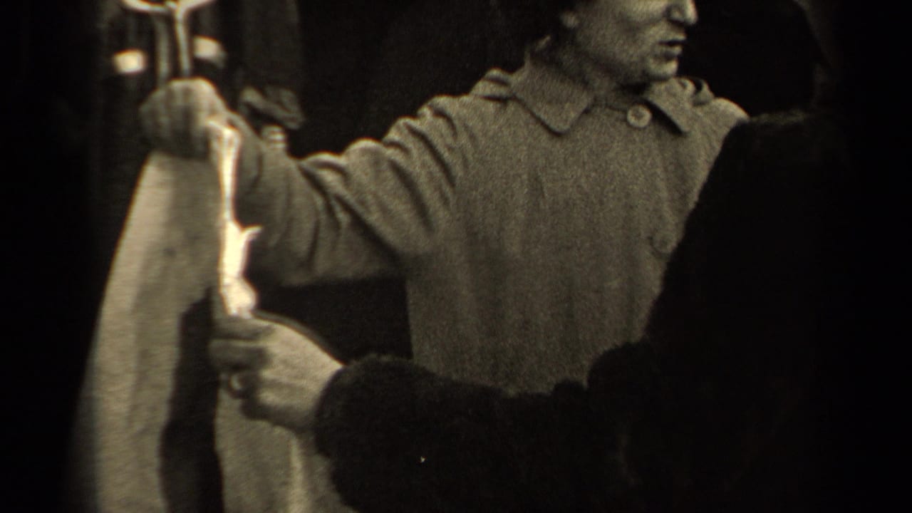 An adult in a light coat holds a shirt with another person in this black-and-white 1947 Paris home-movie frame.