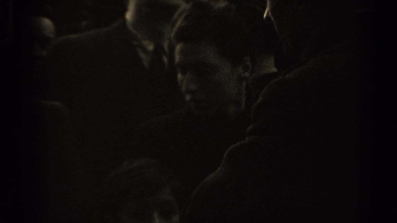 Dark, underexposed view of people crowded close to the camera.