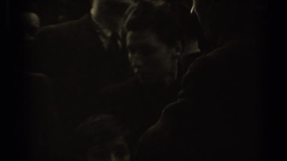 Underexposed 8mm frame from the Paris street clip, with shadowed figures and faces crowded near the camera.