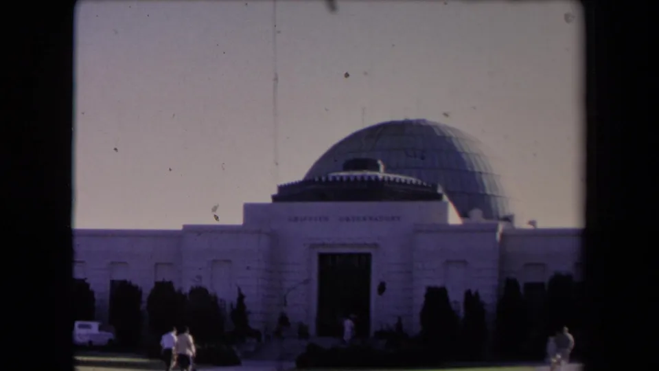 Soft 8mm frame of Griffith Observatory in Los Angeles, with the domed roof, front doorway, shrubs, and visitors in the foreground.