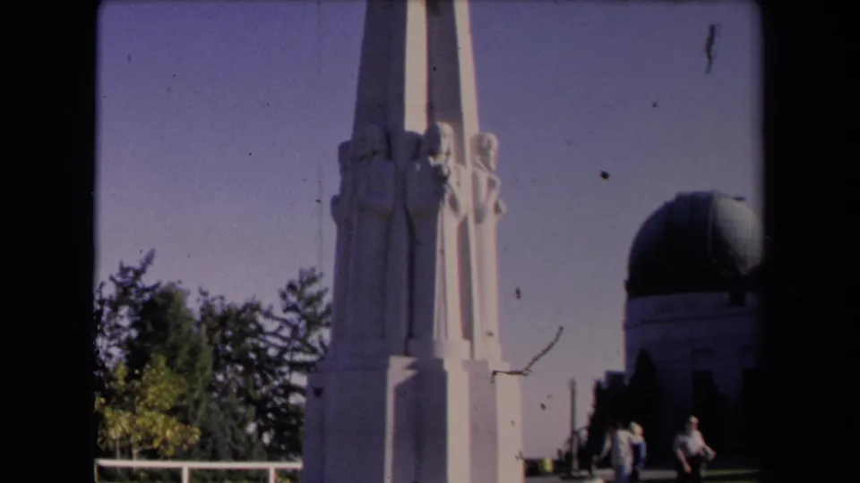 Griffith Observatory grounds in Los Angeles, showing the white sculptural pillar, dome, trees, and small visitor figures in 1967 8mm footage.