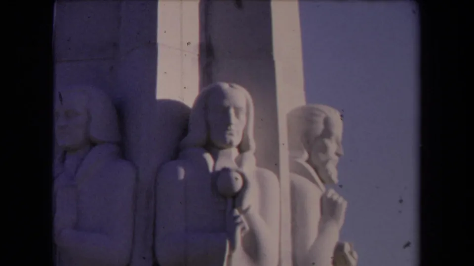 1967 Los Angeles 8mm frame showing close white stone relief figures on a monument, with shadowed carvings and film edge visible.