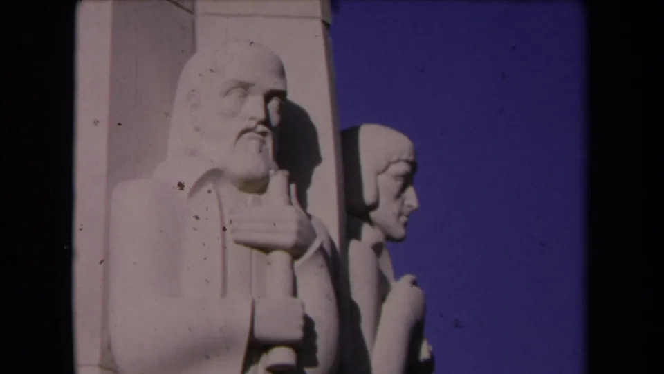 1967 Los Angeles 8mm frame showing a bearded stone figure with staff beside a younger profile figure against blue sky.