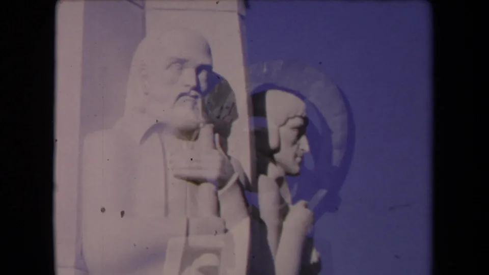 1967 Los Angeles 8mm frame showing the stone figures with a circular form or shadow crossing the blue-sky background.